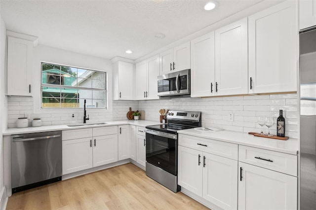 kitchen with tasteful backsplash, stainless steel appliances, white cabinets, light hardwood / wood-style flooring, and sink