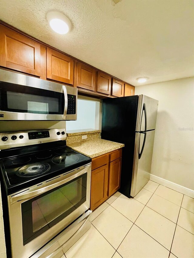 kitchen featuring light tile patterned flooring, a textured ceiling, and stainless steel appliances