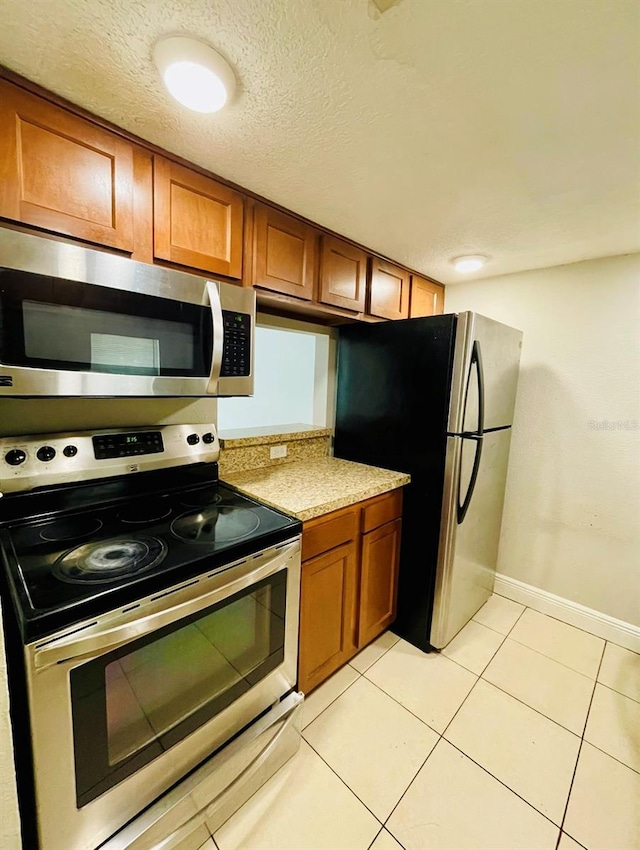 kitchen with light stone countertops, appliances with stainless steel finishes, light tile patterned floors, and a textured ceiling