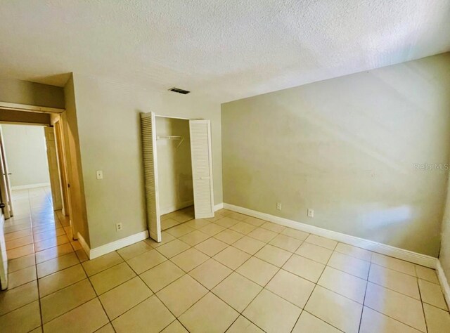 unfurnished bedroom featuring light tile patterned floors, a textured ceiling, and a closet