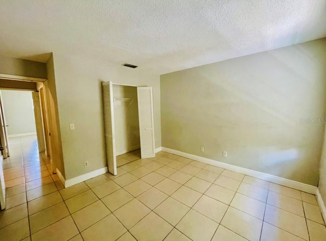 unfurnished bedroom featuring a textured ceiling, a closet, and light tile patterned floors