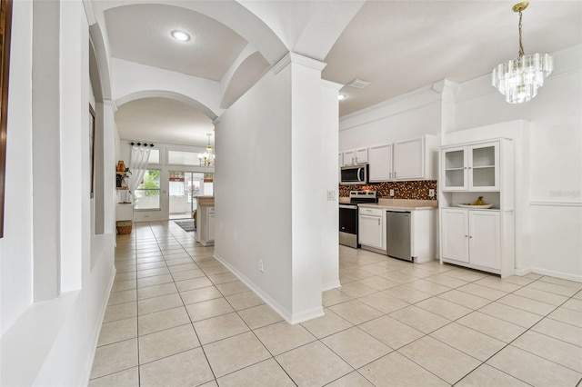 kitchen with appliances with stainless steel finishes, backsplash, light tile patterned floors, an inviting chandelier, and white cabinetry