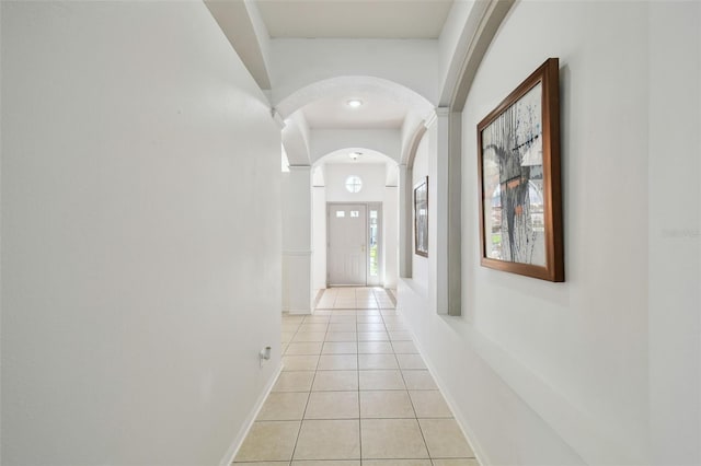 corridor featuring baseboards, arched walkways, and light tile patterned flooring