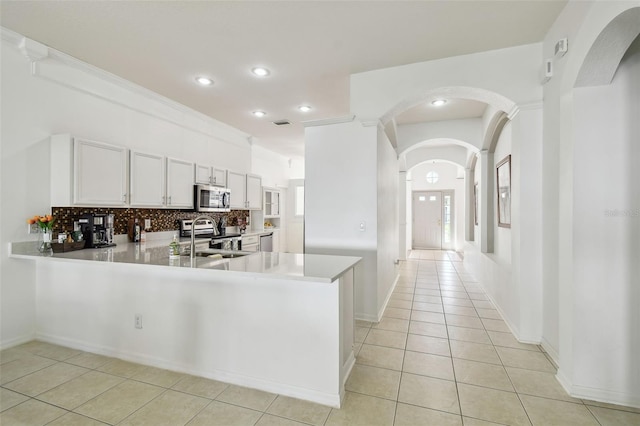 kitchen with arched walkways, appliances with stainless steel finishes, light countertops, a sink, and backsplash