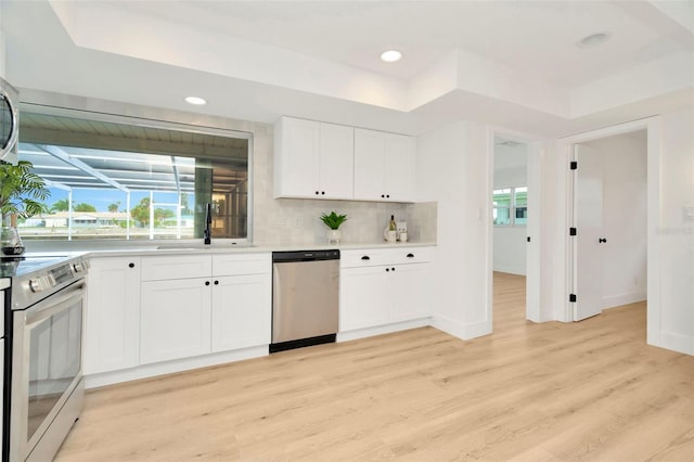 kitchen featuring sink, appliances with stainless steel finishes, white cabinetry, light hardwood / wood-style floors, and a raised ceiling