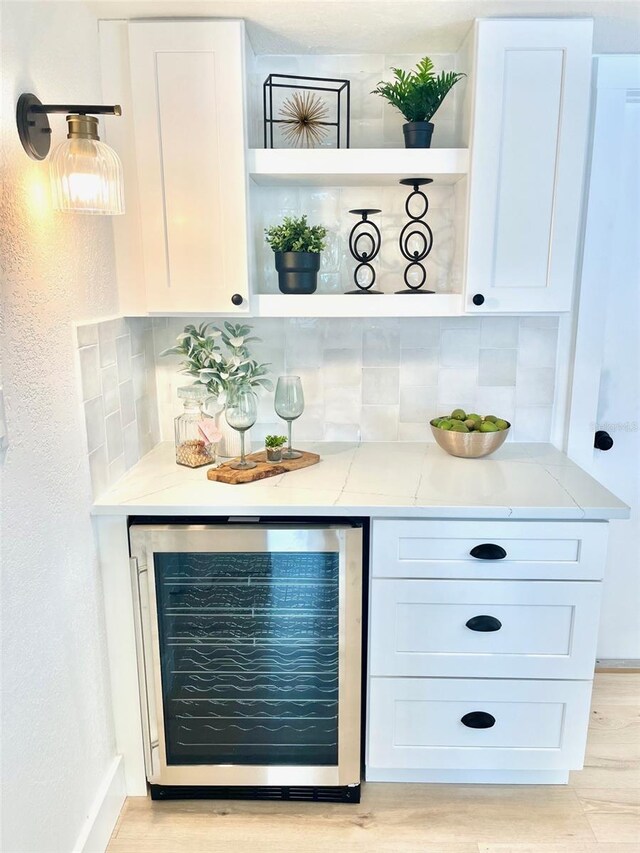 bar with tasteful backsplash, white cabinetry, beverage cooler, and light stone counters