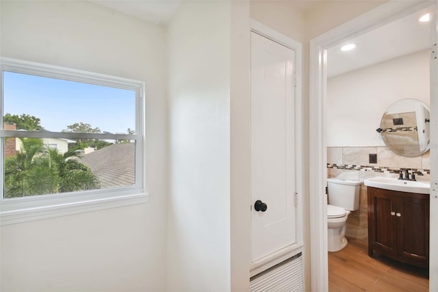 bathroom with toilet, recessed lighting, wood finished floors, vanity, and tile walls