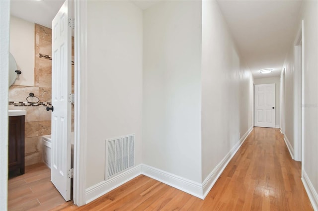 corridor with light wood-type flooring, visible vents, and baseboards