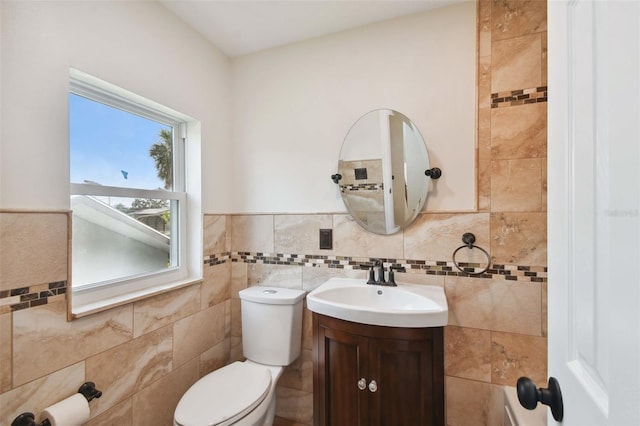 half bathroom with a wainscoted wall, tile walls, toilet, and vanity