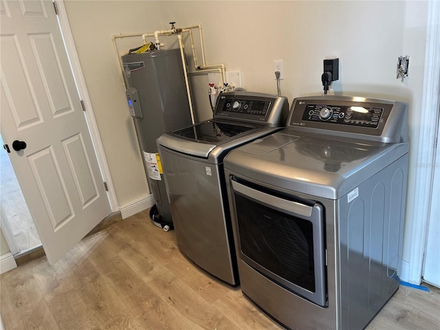 washroom with water heater, washer and dryer, and light hardwood / wood-style flooring