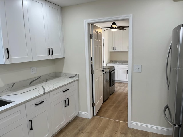 kitchen with light stone countertops, light wood finished floors, white cabinetry, and freestanding refrigerator