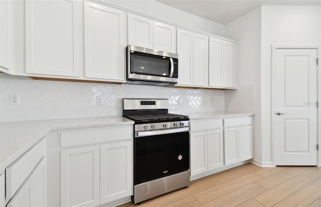 kitchen with light wood-type flooring, appliances with stainless steel finishes, decorative backsplash, and white cabinets