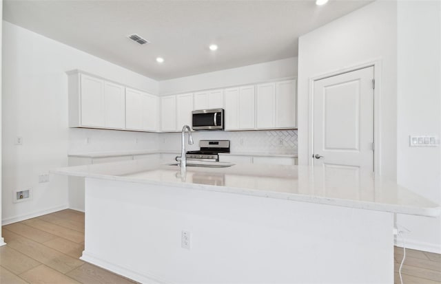 kitchen featuring a spacious island, white cabinetry, light hardwood / wood-style flooring, and stainless steel appliances