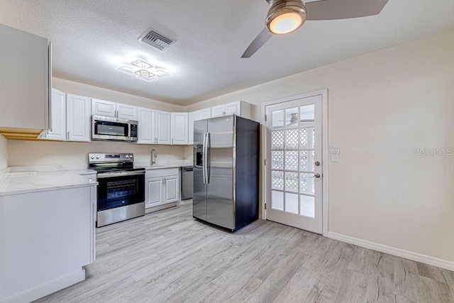 kitchen with light hardwood / wood-style flooring, a textured ceiling, ceiling fan, light stone countertops, and stainless steel appliances