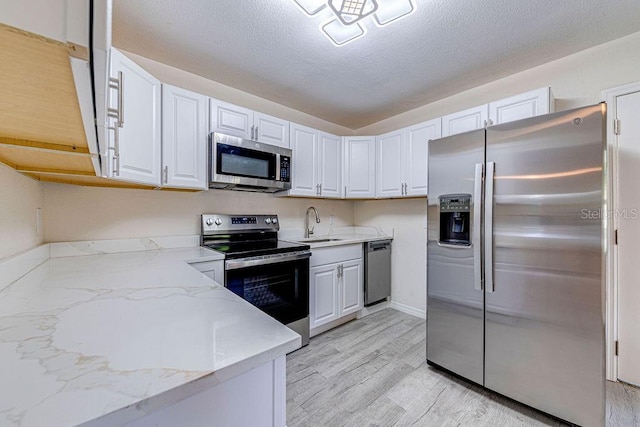 kitchen featuring a textured ceiling, appliances with stainless steel finishes, white cabinetry, light hardwood / wood-style floors, and light stone counters