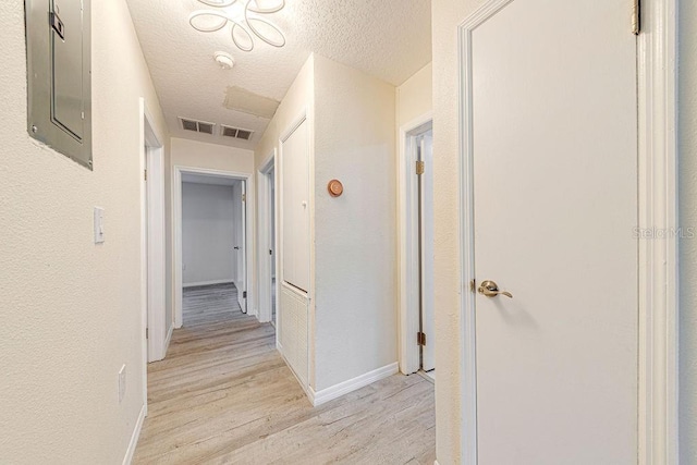 corridor with electric panel, light wood-type flooring, and a textured ceiling