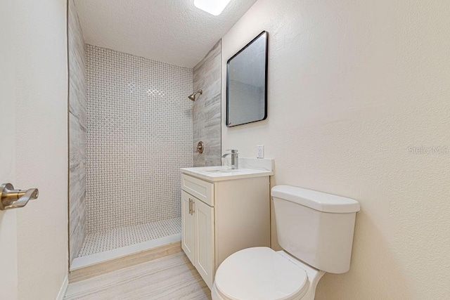 bathroom featuring a textured ceiling, toilet, a tile shower, and vanity