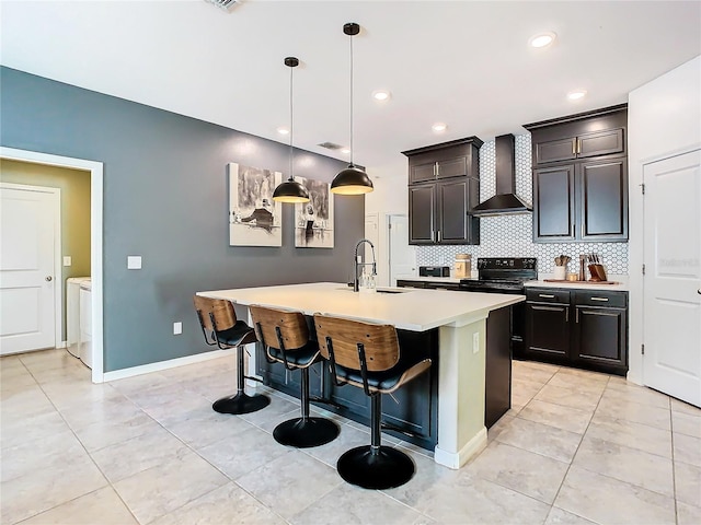 kitchen featuring decorative backsplash, light countertops, washer and dryer, wall chimney range hood, and a sink