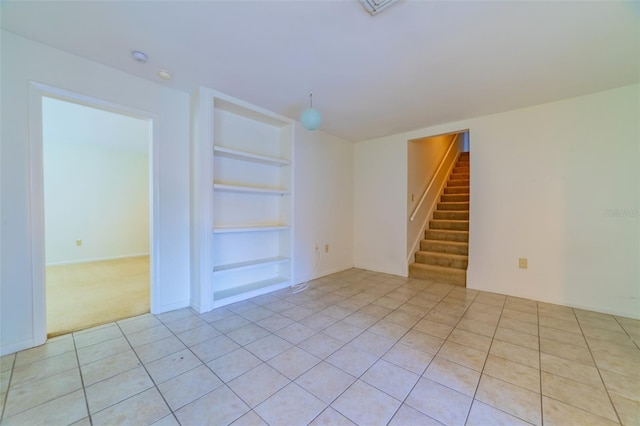 unfurnished room featuring built in features, stairway, and light tile patterned floors