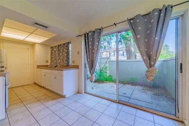 kitchen featuring white cabinets, white refrigerator, sink, and light tile patterned floors