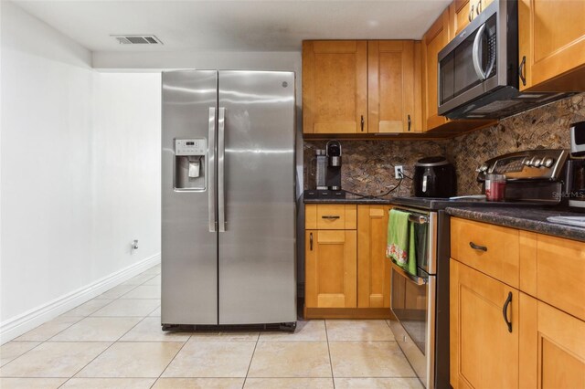 kitchen with light tile patterned flooring, appliances with stainless steel finishes, dark stone countertops, and decorative backsplash