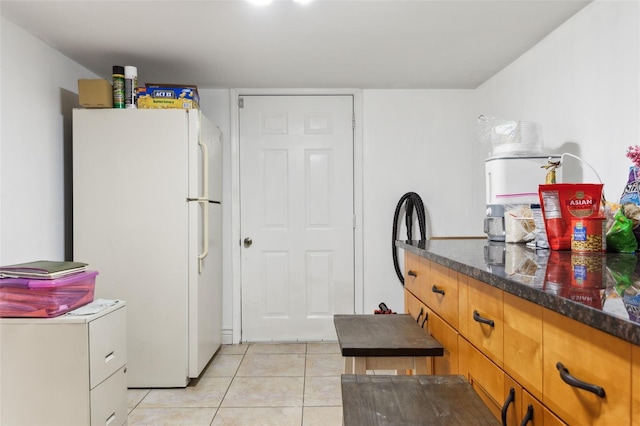 kitchen with light tile patterned flooring, white fridge, and dark stone counters