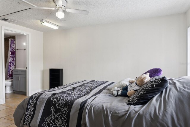 tiled bedroom with ceiling fan, a textured ceiling, and ensuite bath