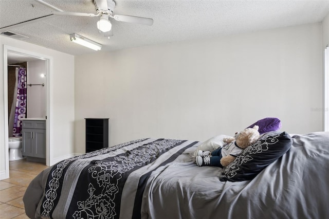 bedroom featuring a textured ceiling, ceiling fan, light tile patterned flooring, visible vents, and ensuite bath