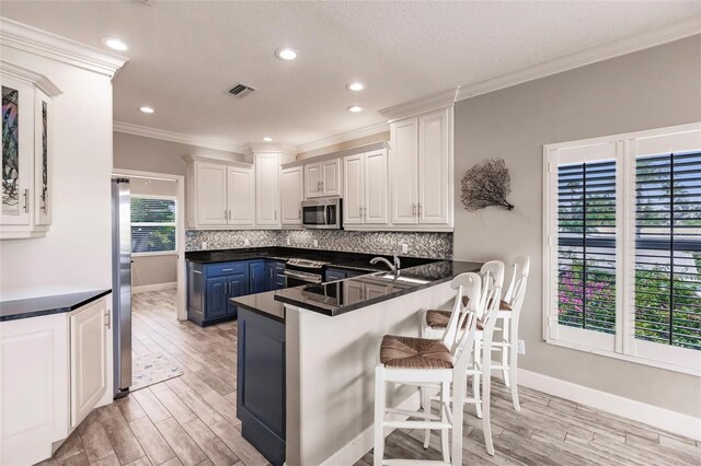 210 Lakeview Dr, Anna Maria, FL 34216 - kitchen with decorative backsplash, white cabinets, stainless steel appliances, light wood-style floors, and a breakfast bar area