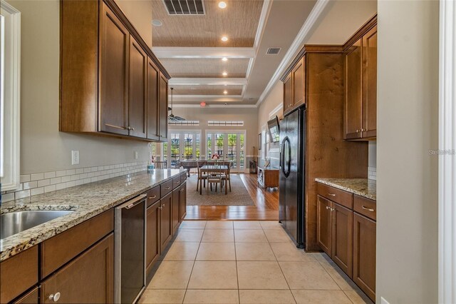 kitchen featuring dishwasher, black refrigerator with ice dispenser, light stone counters, a tray ceiling, and light tile patterned floors