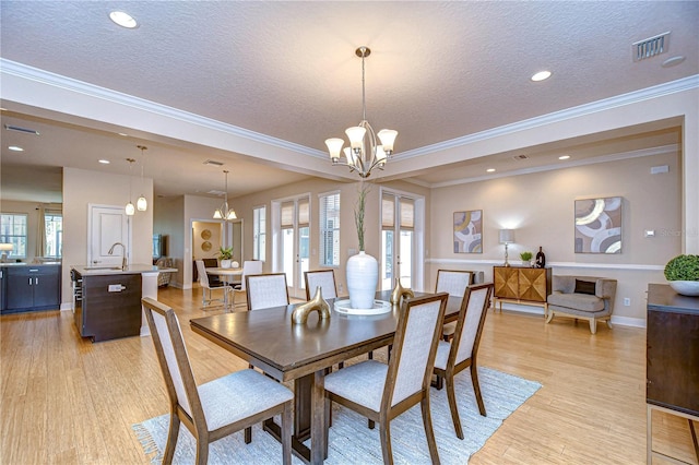 dining room with sink, an inviting chandelier, light hardwood / wood-style flooring, crown molding, and a textured ceiling