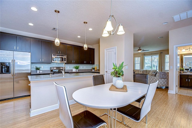 dining area with a textured ceiling, ceiling fan with notable chandelier, sink, and light hardwood / wood-style flooring