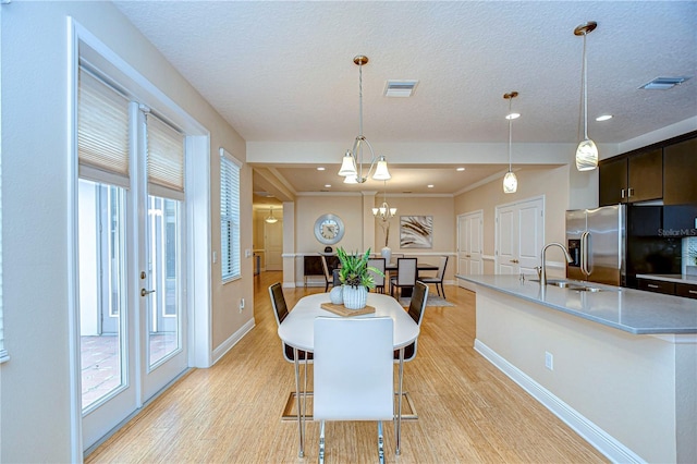 dining area with a textured ceiling, light wood-type flooring, plenty of natural light, and a notable chandelier