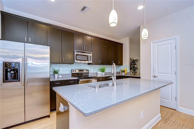 kitchen featuring light stone countertops, appliances with stainless steel finishes, a kitchen island with sink, sink, and pendant lighting