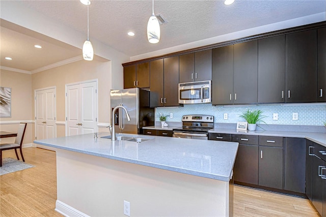 kitchen featuring light stone countertops, light hardwood / wood-style flooring, an island with sink, pendant lighting, and appliances with stainless steel finishes