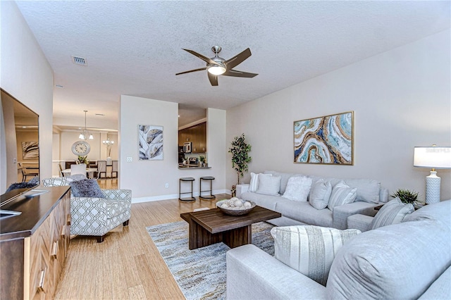 living room featuring ceiling fan with notable chandelier, light hardwood / wood-style floors, and a textured ceiling