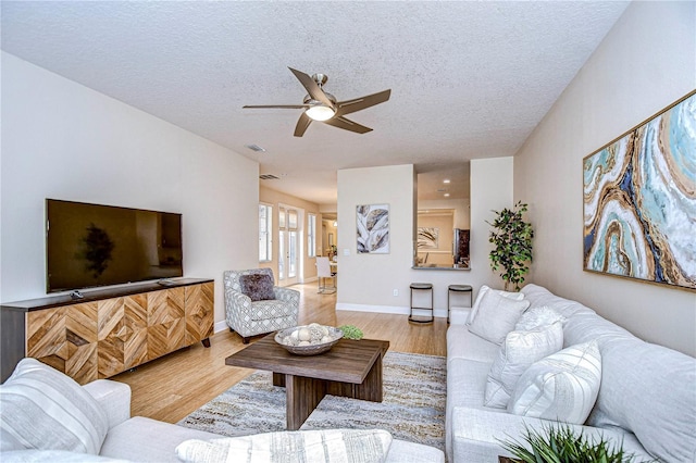 living room featuring ceiling fan, light hardwood / wood-style flooring, and a textured ceiling