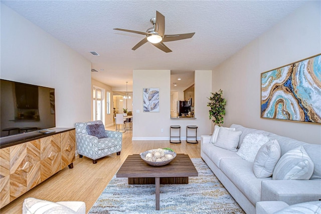 living room featuring ceiling fan with notable chandelier, light hardwood / wood-style floors, and a textured ceiling