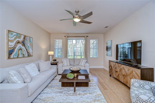 living room featuring ceiling fan, light hardwood / wood-style floors, and a textured ceiling