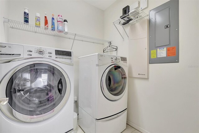 laundry area with electric panel, washing machine and dryer, and light tile patterned floors