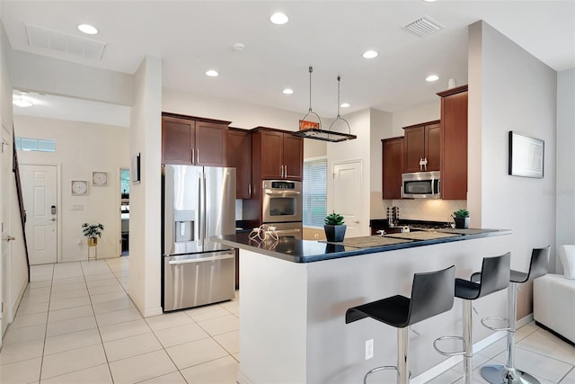 kitchen featuring light tile patterned floors, backsplash, kitchen peninsula, stainless steel appliances, and a breakfast bar