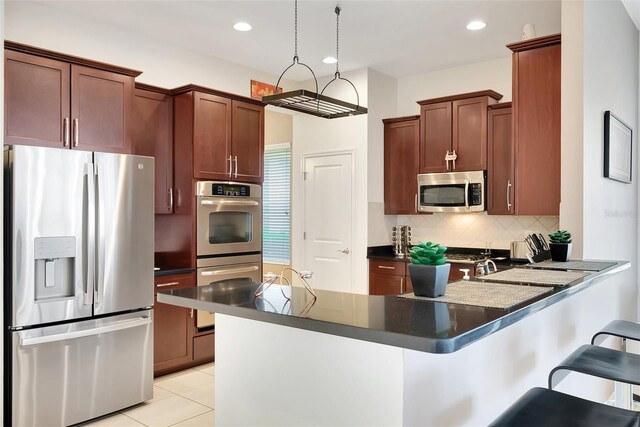 kitchen with dark countertops, a breakfast bar area, backsplash, a peninsula, and appliances with stainless steel finishes
