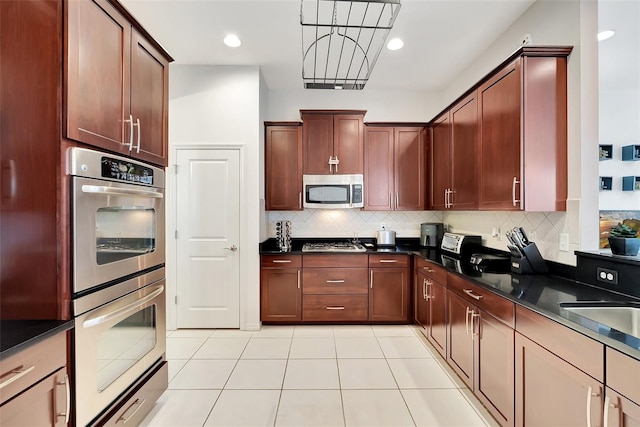 kitchen with light tile patterned floors, appliances with stainless steel finishes, backsplash, dark stone countertops, and decorative light fixtures