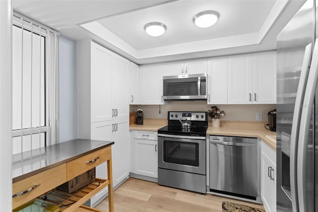 kitchen with light hardwood / wood-style flooring, appliances with stainless steel finishes, a raised ceiling, and white cabinets