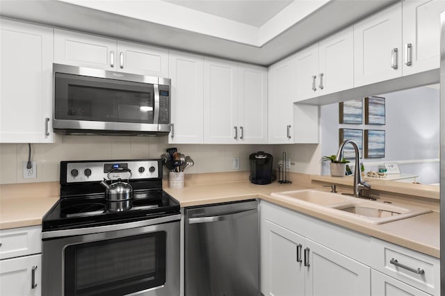 kitchen with a raised ceiling, appliances with stainless steel finishes, white cabinetry, tasteful backsplash, and sink