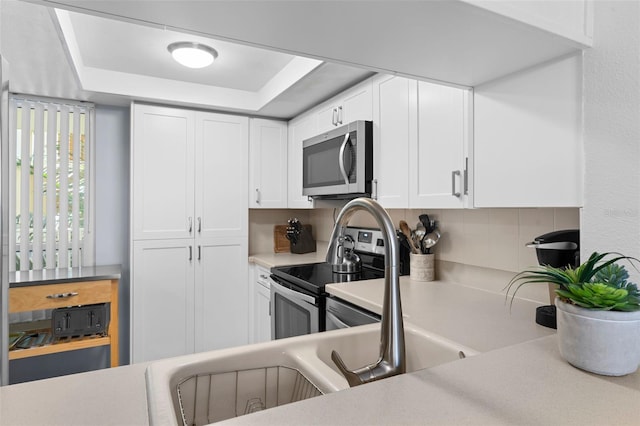 kitchen featuring appliances with stainless steel finishes, a raised ceiling, tasteful backsplash, and white cabinetry