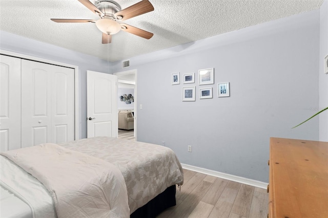 bedroom featuring ceiling fan, a textured ceiling, light hardwood / wood-style floors, and a closet