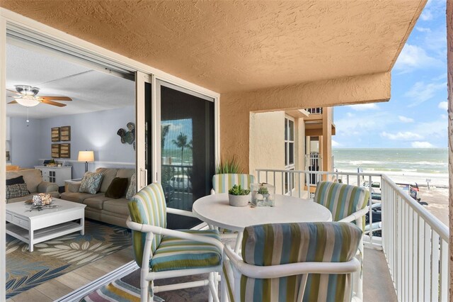 balcony featuring ceiling fan, a beach view, a water view, and an outdoor living space