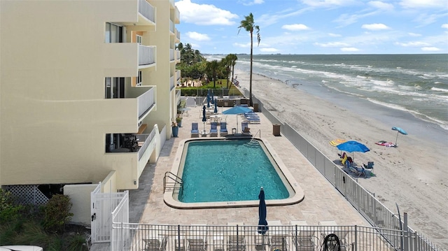 view of pool with a patio, a water view, and a beach view