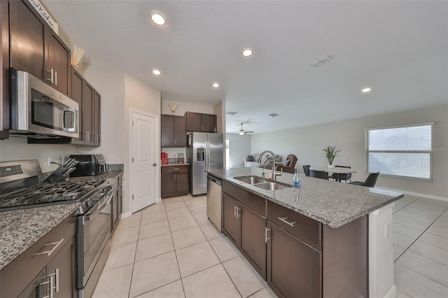 kitchen featuring ceiling fan, appliances with stainless steel finishes, light stone countertops, an island with sink, and sink